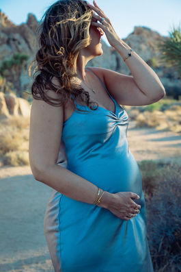 Pregnant woman in blue dress touching hair in desert light, Joshua Tree maternity photo near Palm Springs