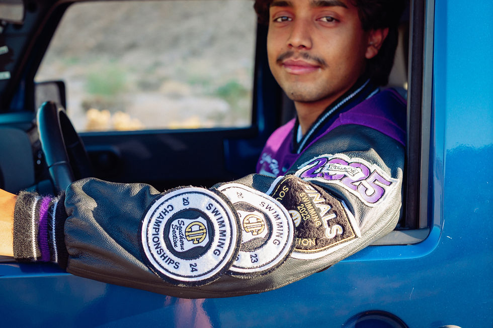 High school senior standing beside his 2009 Jeep Wrangler with mountains and sunset behind him, wearing his letterman’s jacket. Captured by a Palm Springs senior photographer, Joshua Tree senior portraits.