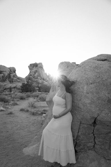 Black and white maternity portrait of smiling pregnant woman holding baby bump in Joshua Tree National Park near Palm Springs