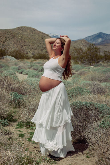 Pregnant woman in white skirt and tank top standing in desert at Mission Creek Preserve near Joshua Tree
