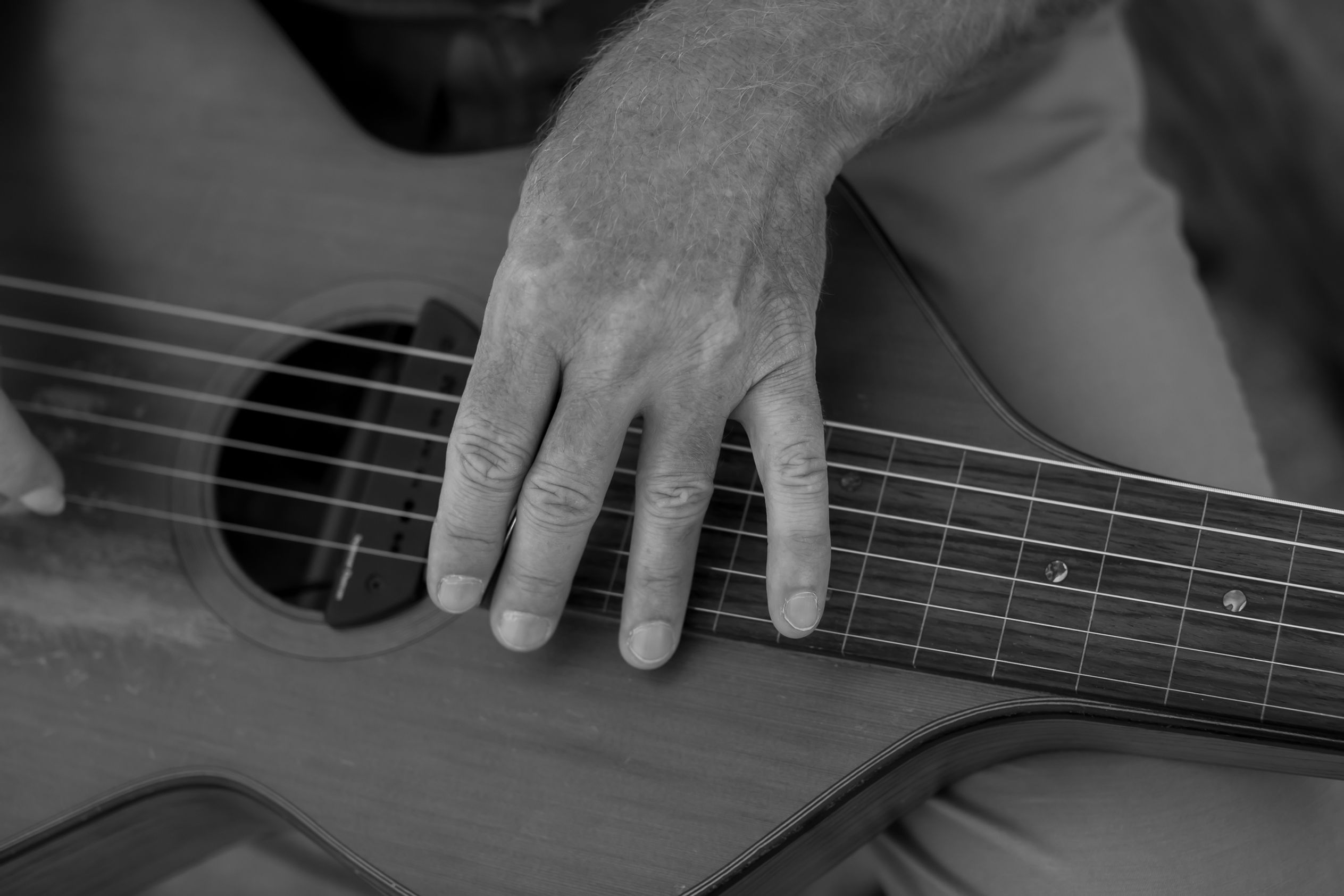 Close-up black and white photo of a groom’s hand on guitar before ceremony at Sacred Sands. Joshua Tree wedding detail captured in 35mm film style.