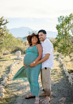 Near Palm Springs. Maternity portrait of parents-to-be standing together on a desert path with hands on the baby bump at Kaleidoscope Desert Animal Sanctuary in Morongo Valley