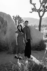 Black-and-white portrait of a couple holding hands beneath Joshua trees and beside granite boulders during a couples photography session at Cap Rock in Joshua Tree National Park.