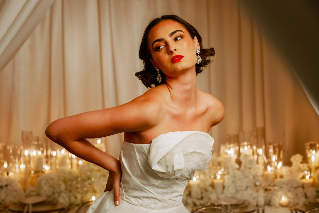 Bride at candle-lit wedding table with white florals, glass decor, and ruffled Karen Sabag gown—San Diego bridal editorial.