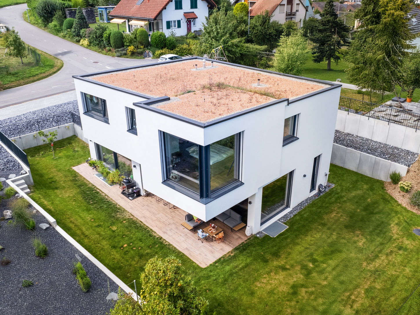 Luftbild eines modernen weissen Einfamilienhauses mit Flachdach, Garten und Umgebung.