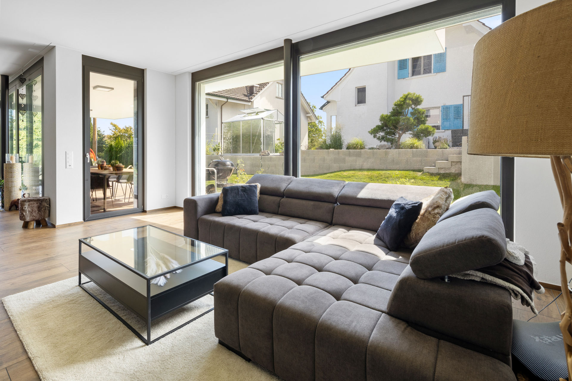 Wohnzimmer mit grauem Ledersofa, Glascouchtisch und Schiebetüren zum Garten.