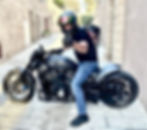 A man wearing a helmet sits on a motorcycle in a stone alleyway and gives a thumbs-up.