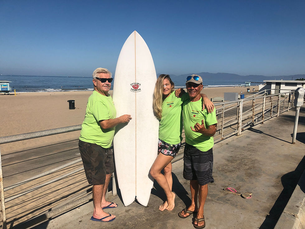 Thumbnail: Three people in green shirts with surfboard on beach