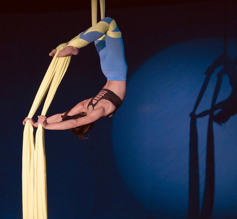 Aerial acrobat doing a scorpion with blue pants on a blue background
