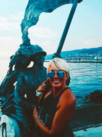About me: Helena smiling by a statue by the sea.