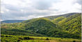Lush green rolling hills and mountains under a cloudy sky.