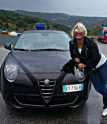 Helena smiling, leaning on black car with blue light