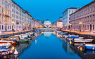 Canal with boats, illuminated buildings, and church at dusk.