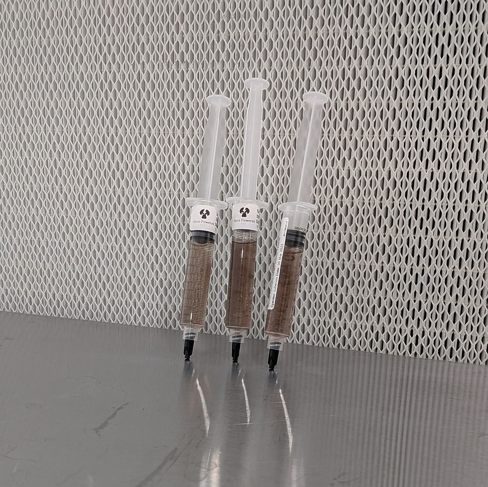 Three clear syringes full of spores on a metal table against a white mesh background; labels read Myco Powered LLC.