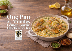 A rustic skillet of lemon garlic chicken and creamy orzo sits on a wooden table, garnished with fresh parsley, lemon slices, and parmesan, with olive oil and small bowls of herbs nearby in soft natural light.