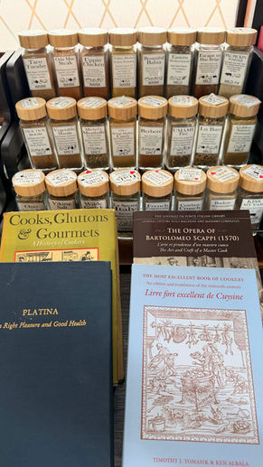 Historic culinary books including Platina and Scappi displayed behind jars of Oak City Spice Blends, representing the connection between Renaissance cooking manuscripts and modern spice craft.
