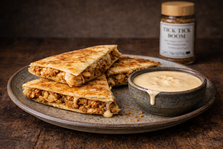 Golden brown chicken quesadillas seasoned with Tick Tick Boom spice blend, plated with creamy homemade queso on a rustic wooden table.