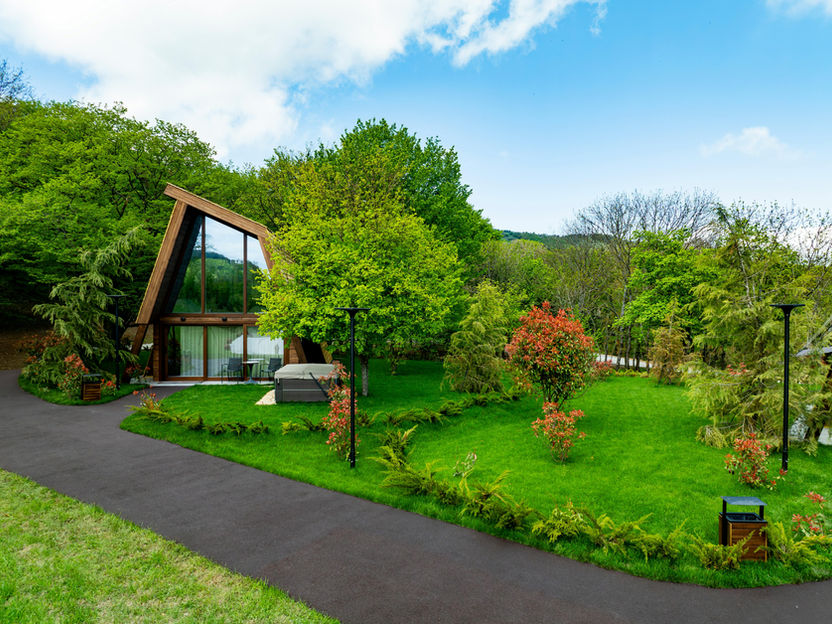 Nowoczesny dom we wzgórzach, zielony trawnik, asfaltowa ścieżka, błękitne niebo.