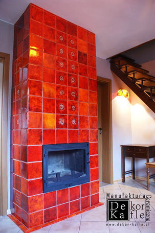 Aranżacja salonu z wysokim aż po sufit kominkiem. Obudowa wkładu kominkowego wyłożona ręcznie robionymi, ceramicznymi kaflami w kształcie kwadratu o wymiarach 15x15 cm. Producent: Manufaktura Dekor-Kafle. Płytki kominkowe pokryte błyszczącym, cieniowanym szkliwem w intensywnym kolorze Ognisty Pomarańcz. W centralnej części wmurowano pojedyncze kafle dekoracyjne z subtelnym, tłoczonym wzorem zduńskim. Ognioodporna ceramika akumulująca ciepło, luksusowe wykończenie salonu, tradycyjne rzemiosło.