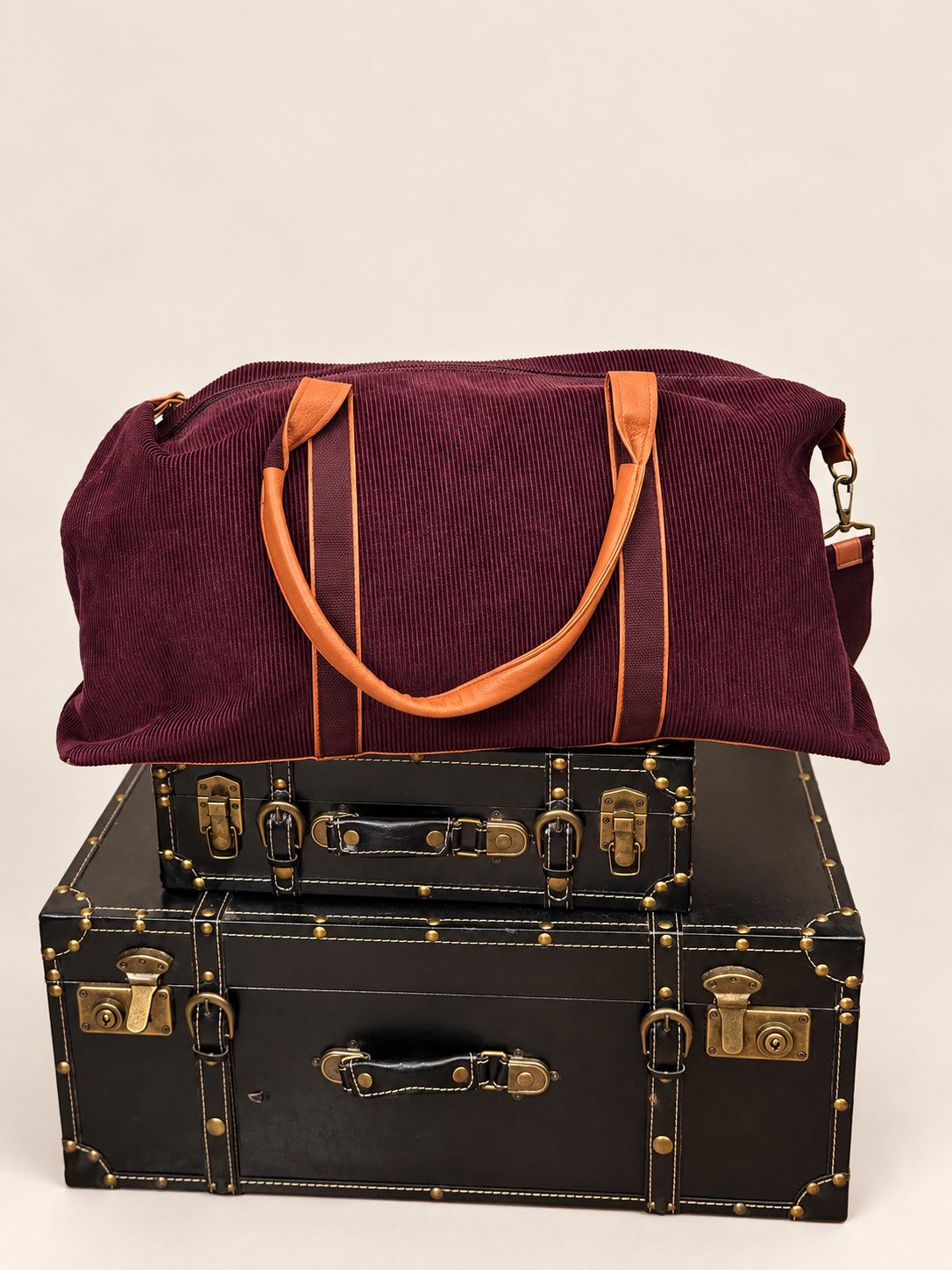 DSW burgundy corduroy duffle bag with cognac-tone handles displayed on vintage trunks