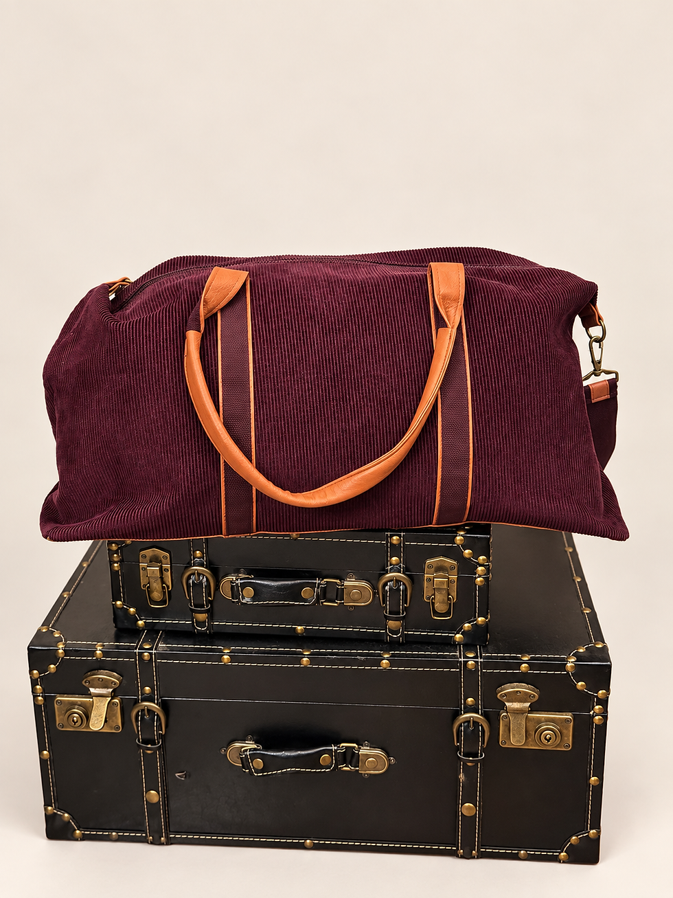 DSW burgundy corduroy duffle bag with cognac-tone handles displayed on vintage trunks