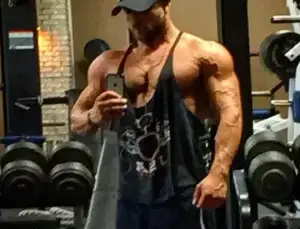 Muscular man in gym free weights wearing stringer tee shirt and baseball cap