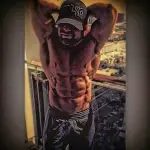 Muscular man stretches on a balcony, wearing a cap and shorts. Cityscape in background. Moody lighting with a strong contrast effect.