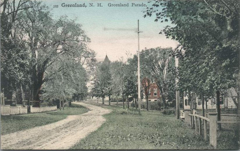 Hand-tinted vintage postcard of a tree-lined dirt road through Greenland's town center, with white picket fences, a utility pole, a red brick building and a church steeple in the distance. Printed title reads "183 Greenland, N.H. Greenland Parade."
