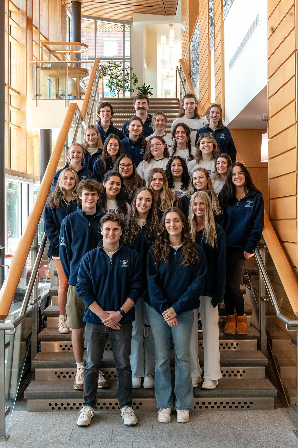 The Voice Z Digital team poses on a staircase in navy and white branded apparel at UNH's Paul College.