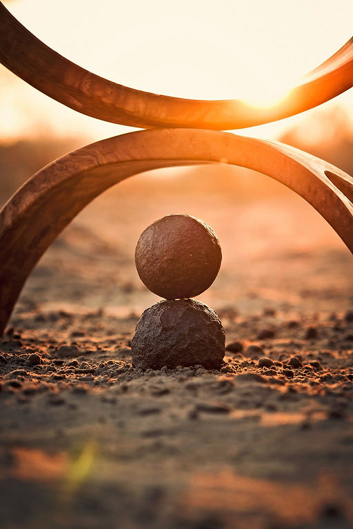 Two rocks balancing under an arch with a golden sunset on a sandy ground