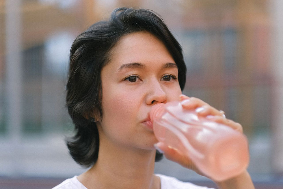 Young woman drinks from a pink bottle outdoors, close-up with a soft blurred background and calm expression.