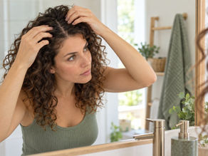 Femme aux cheveux bouclés observant doucement son cuir chevelu dans un miroir