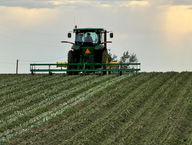 Green John Deere tractor plowing a field, under cloudy sky, farming.