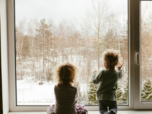 Two children looking out a home window at a snowy winter landscape