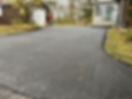 Freshly paved asphalt driveway being finished by worker using tamper