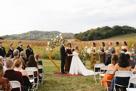 Wedding party and guests look on as a bride and groom are married in front of an outdoor octagonal arch.