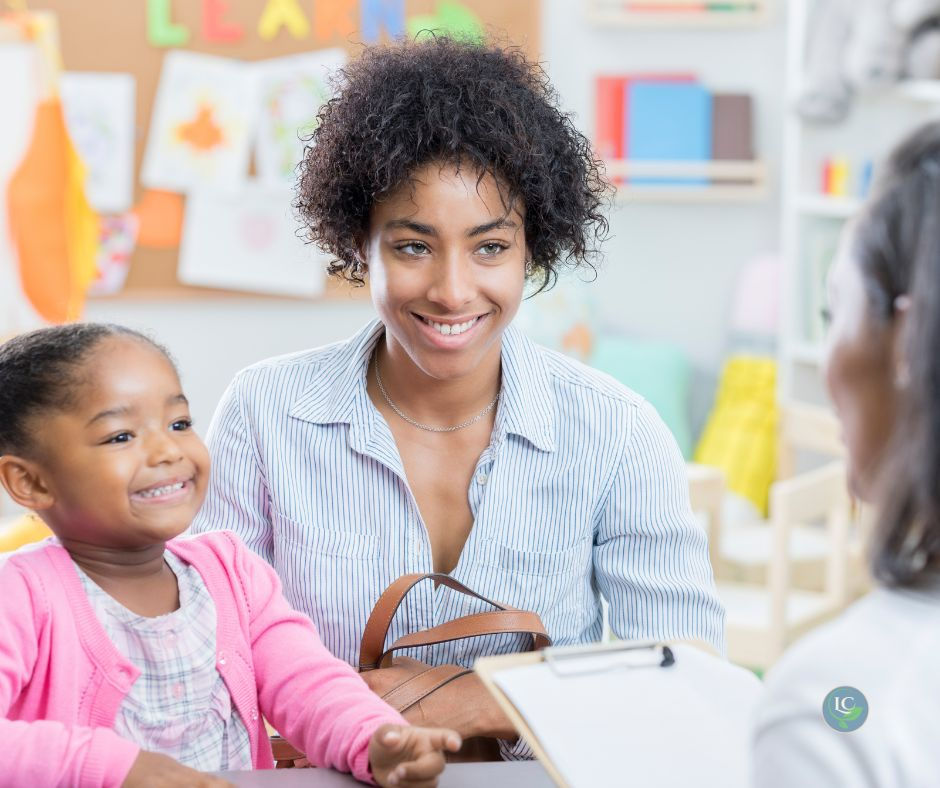A close up of a young girl and her mother sitting in a classroom talking to a teacher.