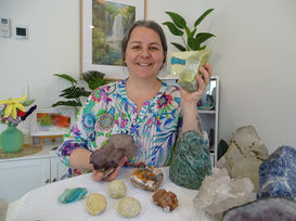 Woman with gems and plant, smiling and holding a stone container.