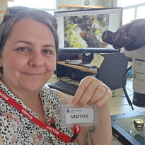 Woman holds visitor tag near microscope, computer with a squirrel image.