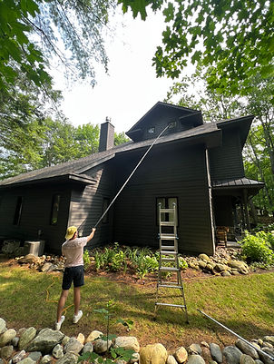 Professional window cleaner using an extension pole to clean high windows on a dark cottage in Muskoka