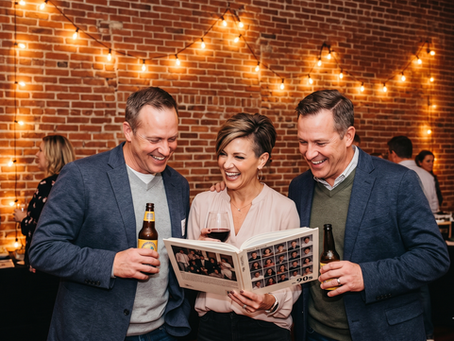 Three smiling adults at a brick-walled party read a yearbook with 90s photos, holding beer under string lights.
