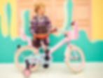 Meisje staat naast roze supersuper kinderfiets bij kleurrijke muur.jpg