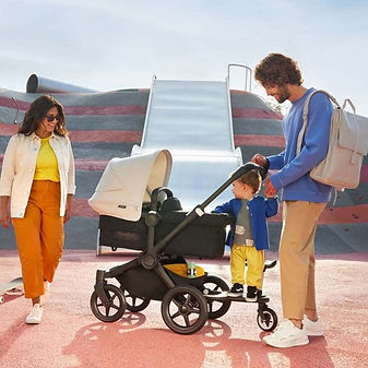 Hippe familie in kleurrijk speeltuin met bugaboo kinderwagen en kind op meerijdplankje.jpg