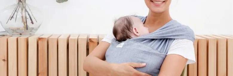 Mutter sitzt auf Bank mit Baby im Tragetuch.webp