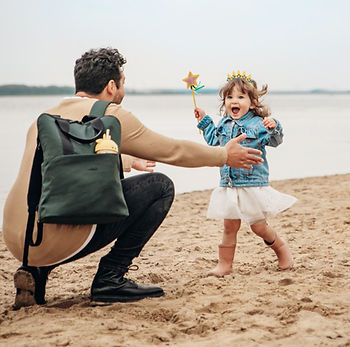 Vater mit Joolz-Windelsack-Rucksack und Kind zusammen glücklich am Strand