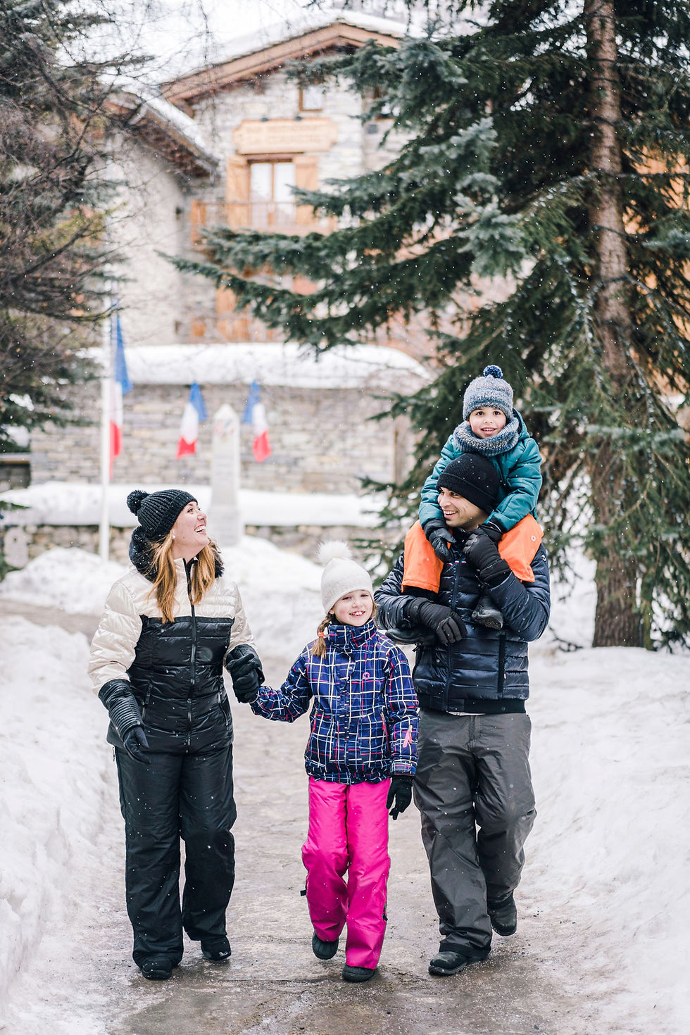 En glad familie spaserer gjennom en snødekt landsby i Alpene under vinterferien sin, pakket inn i fargerik vinterutstyr og nyter den friske, festlige atmosfæren.