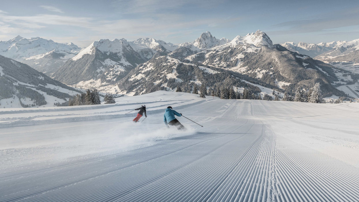 Skikjørere som suser ned de perfekt preparerte alpinbakkene i Gstaad, Sveits, med majestetiske fjell og vakre snødekte landskap i bakgrunnen