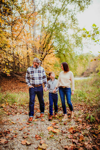 family walks on river side surrounded by fall leaves in full bright yellow colors