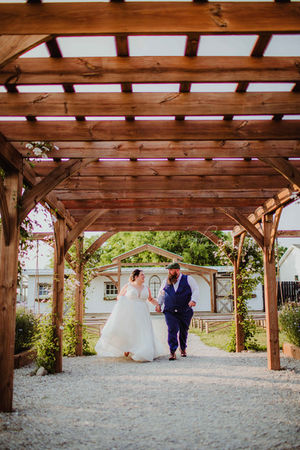 plus size Blossom Barn bride and groom walking under wedding arbor during summer wedding ceremony