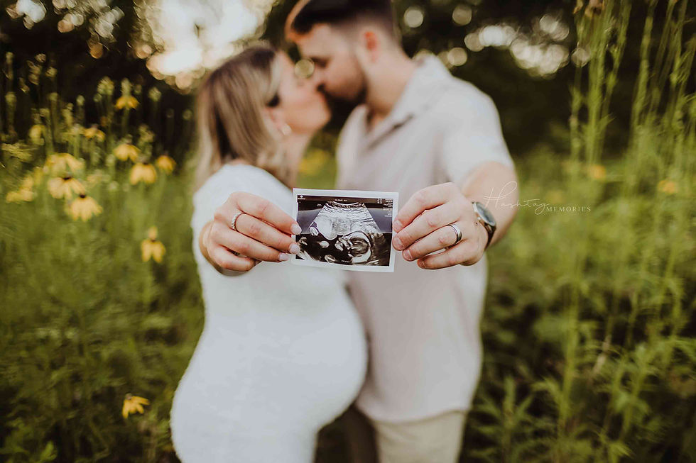 Pregnant couple kisses in a flower field, holding an ultrasound photo toward the camera; Hashtag Memories watermark.